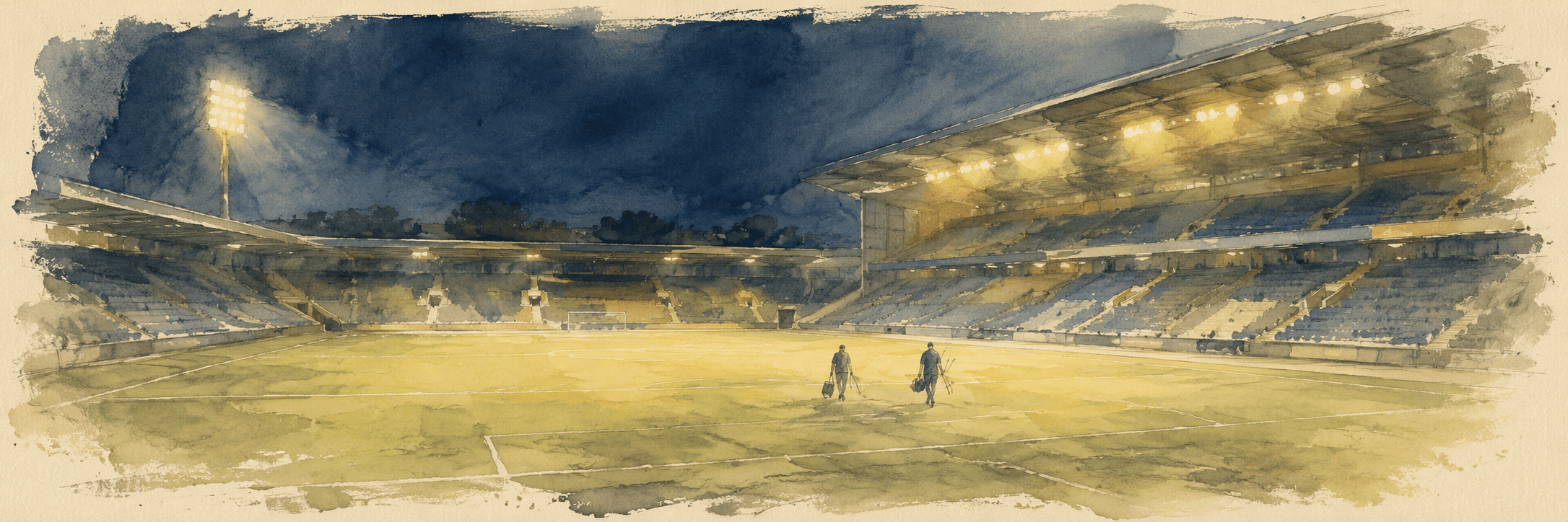 Empty floodlit stadium after a match, two ground staff walking out